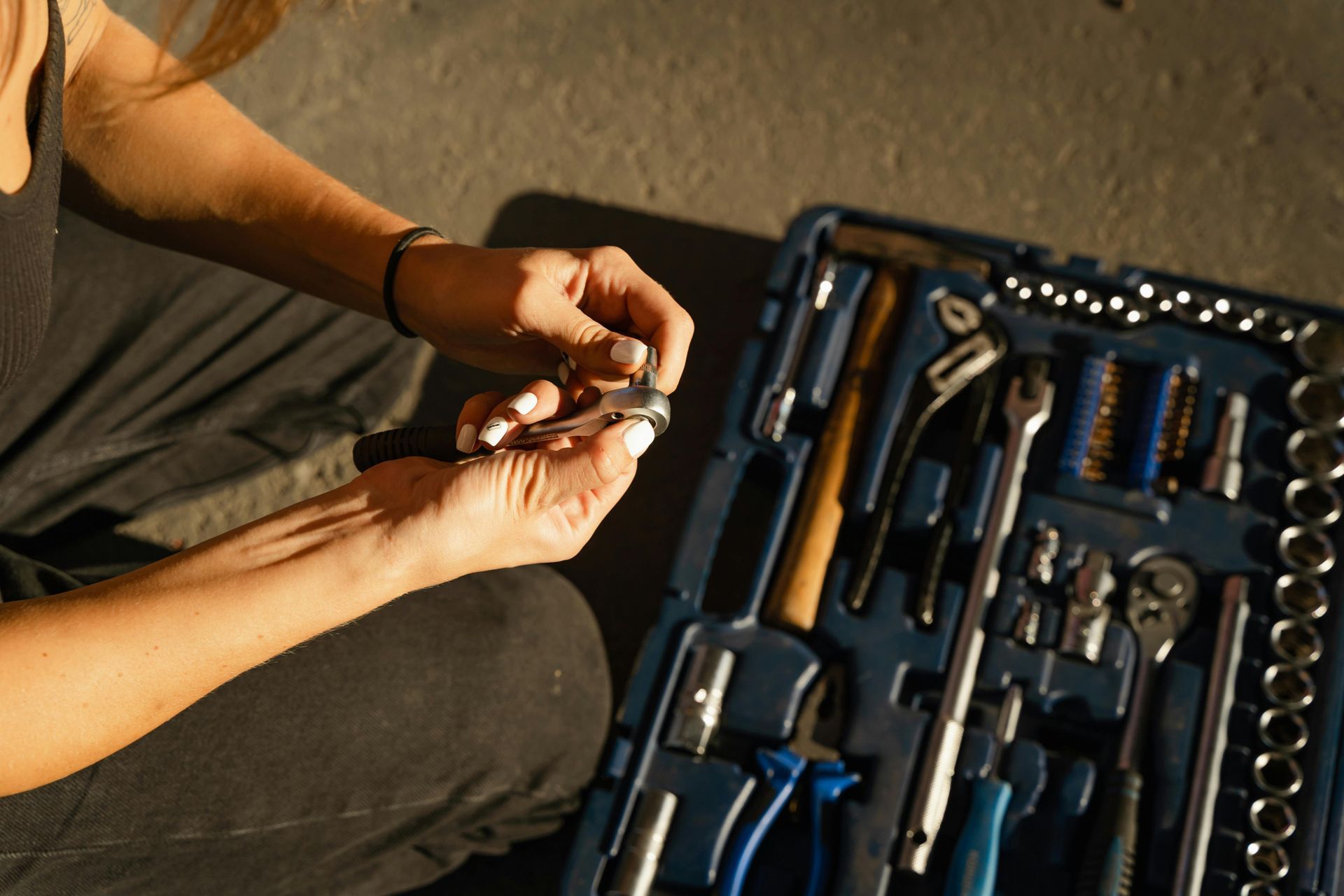 Person holding a wrench, examining it near an open tool kit. Sunlight highlights the scene.