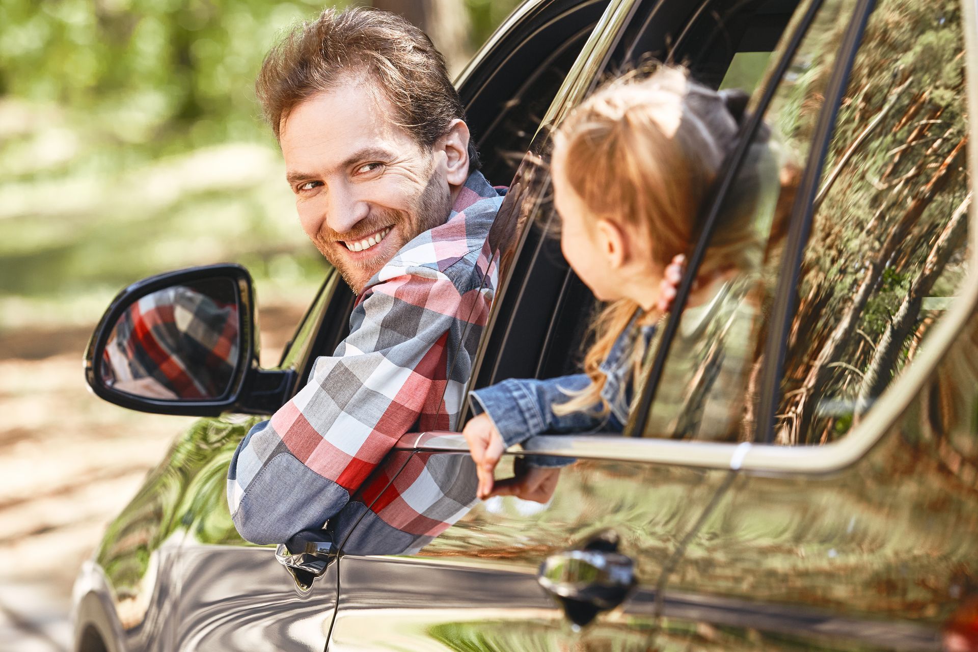 Man smiles at a child from a car window; outdoors in sunlight.