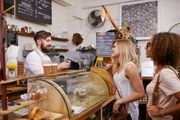 A barista takes an order from two customers at a cafe counter.
