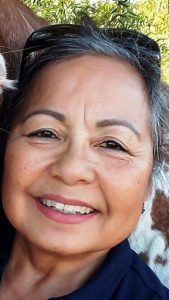 Smiling woman with short gray hair and sunglasses on head, outdoors.