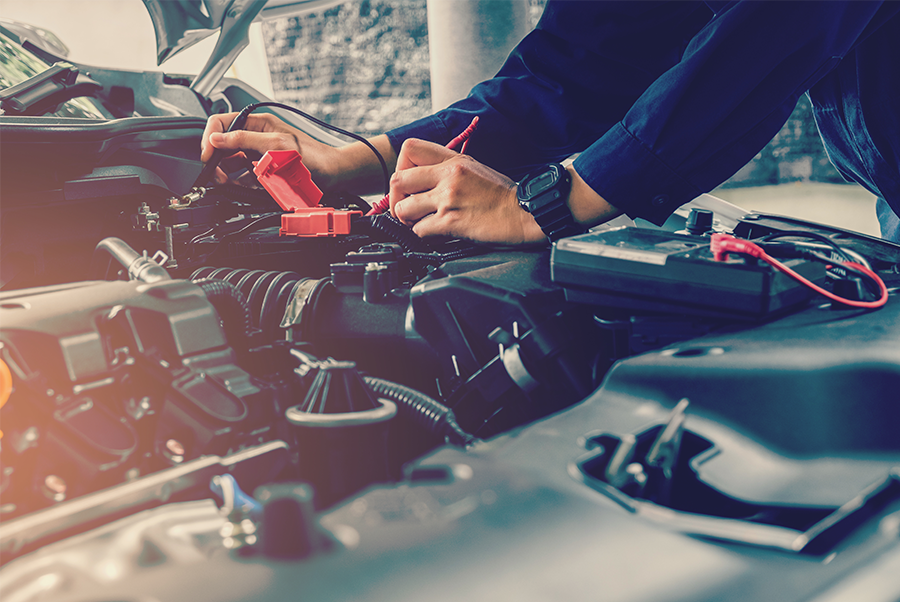 Mechanic using jumper cables on a car battery in an open engine bay