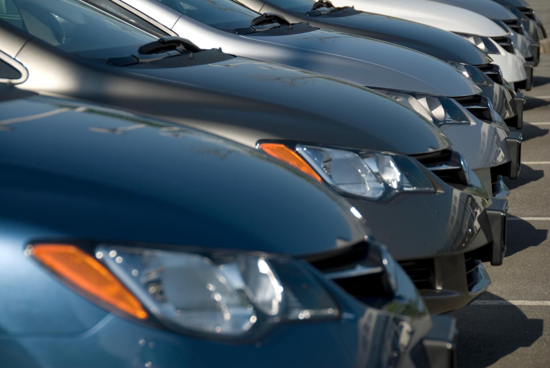 Row of parked dark blue cars seen from the front in a dealership lot