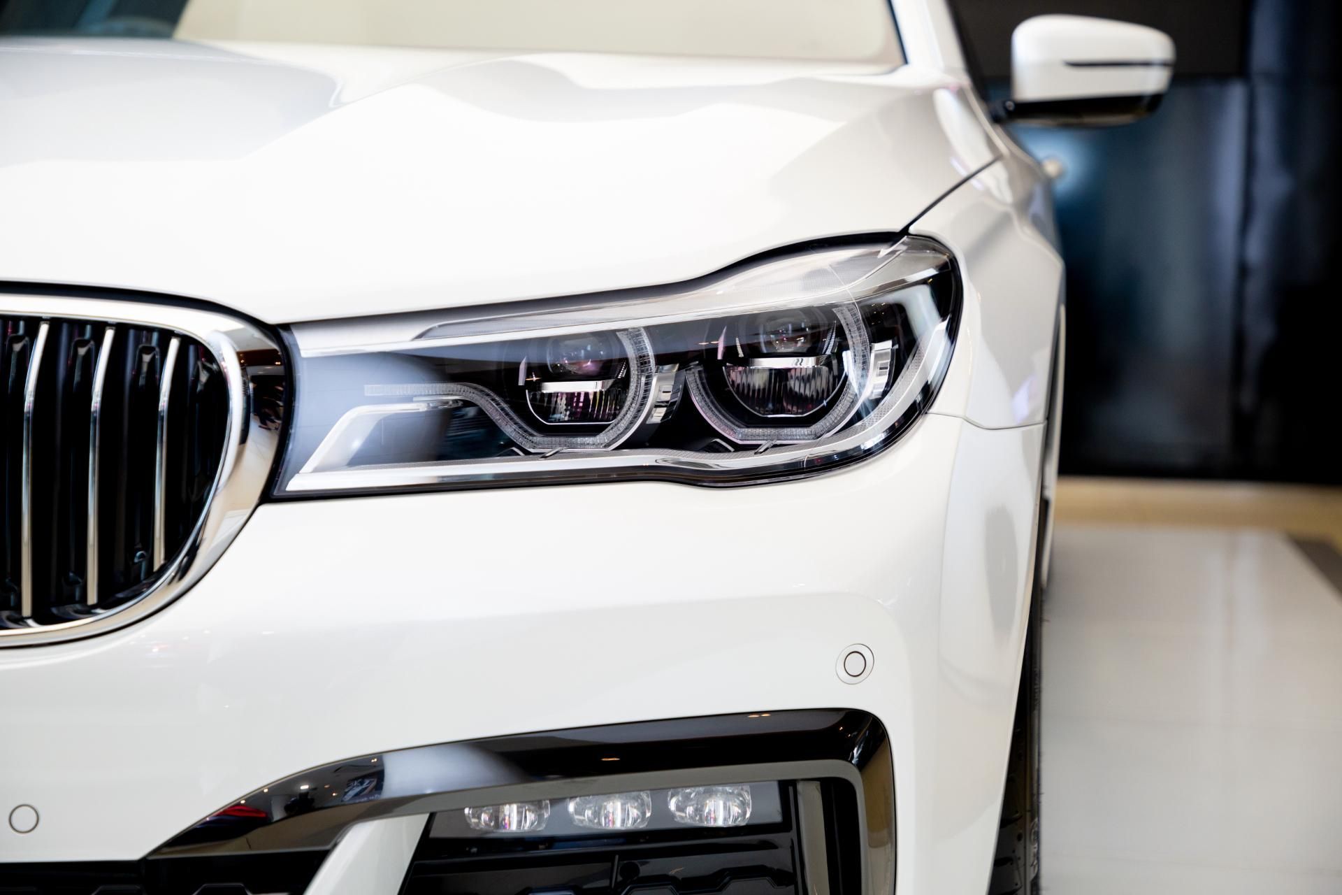 Close-up of a white luxury car’s front grille and headlight in a showroom