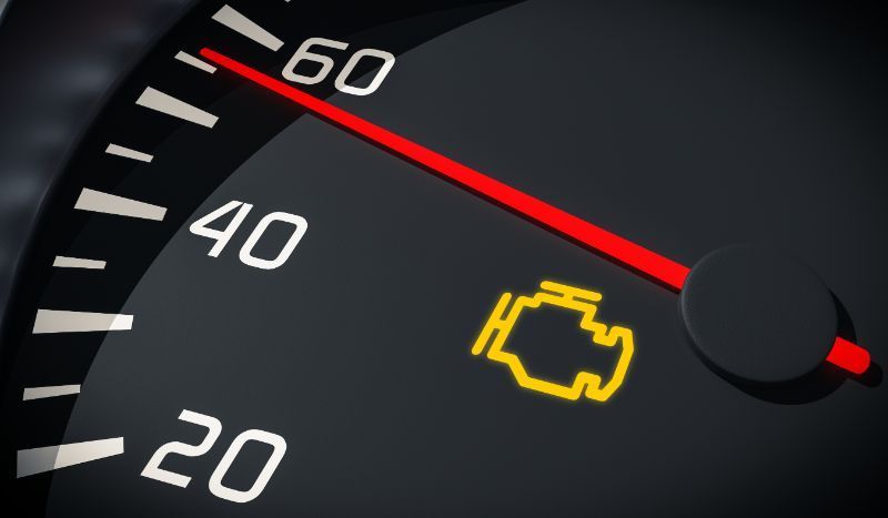 Car dashboard gauge with red needle and yellow check engine warning light