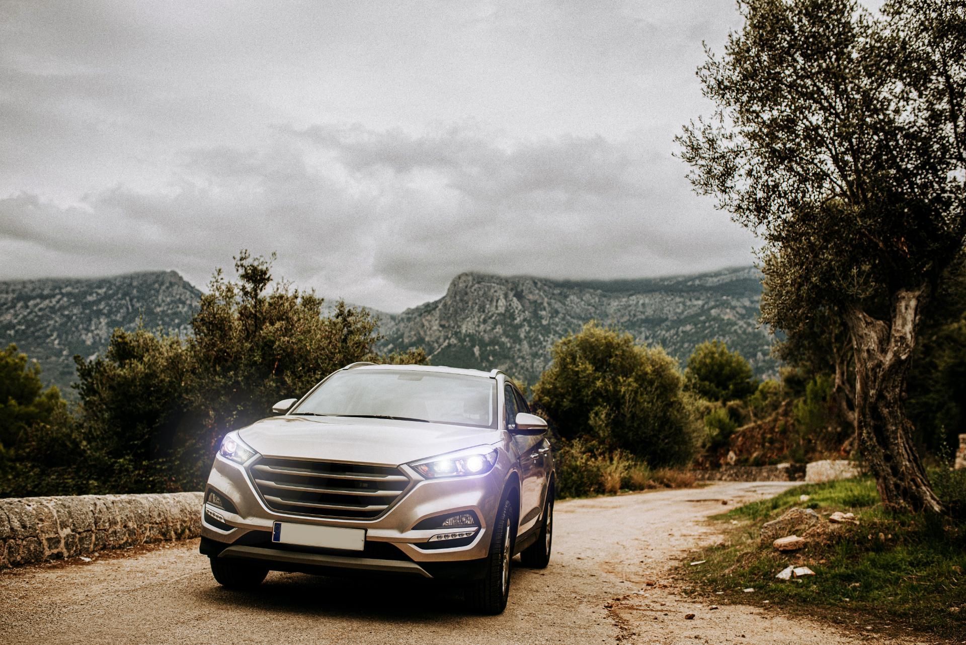 Silver car on a winding dirt road in a mountainous landscape with cloudy sky