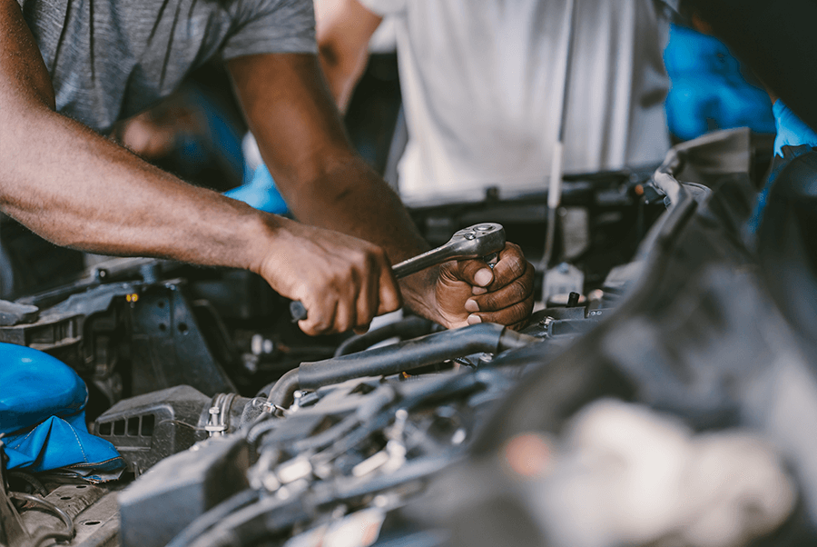 Mechanic working under a car hood with tools in a garage