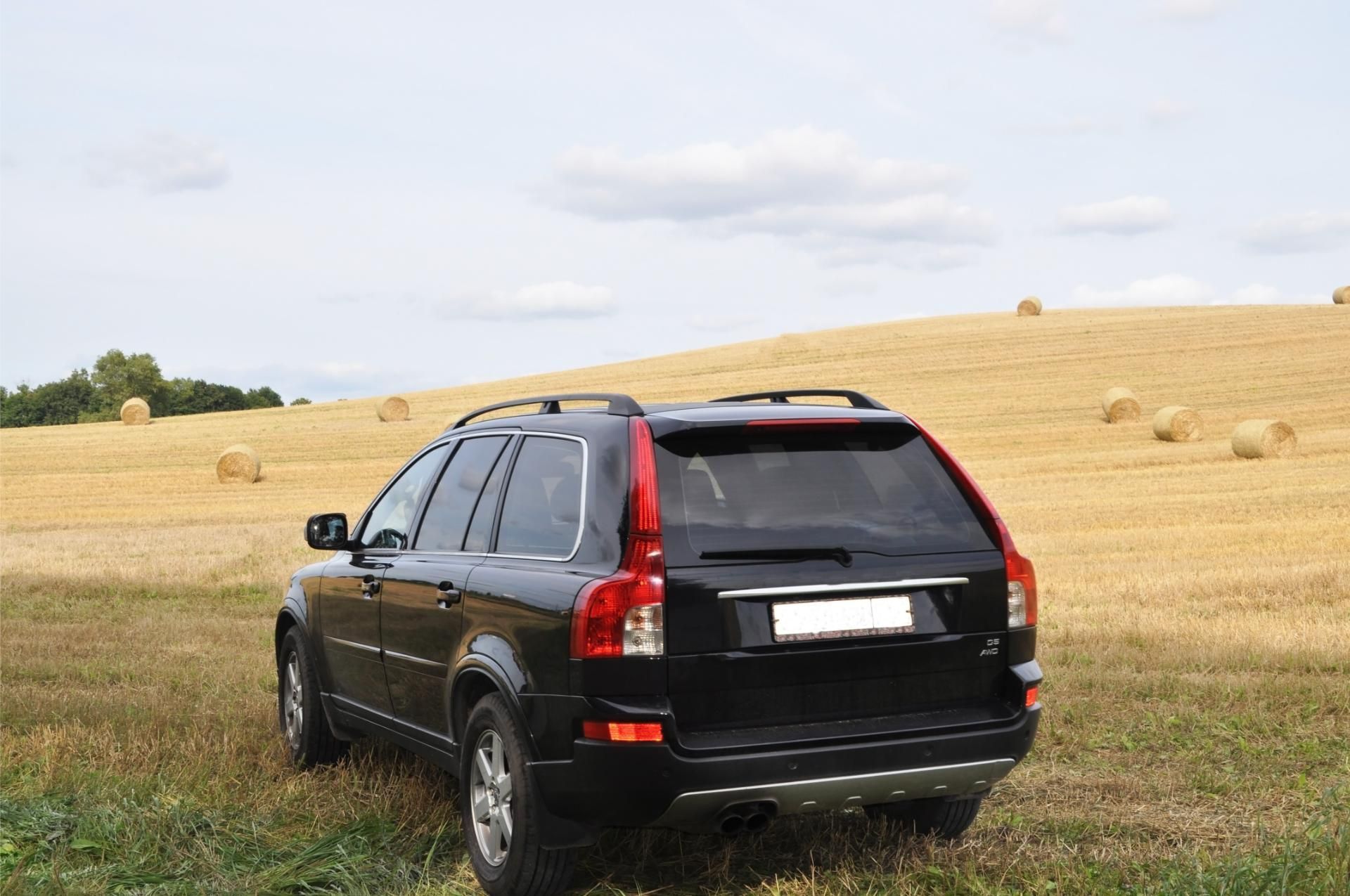 Black SUV parked in a grassy field near golden hay bales under a cloudy sky