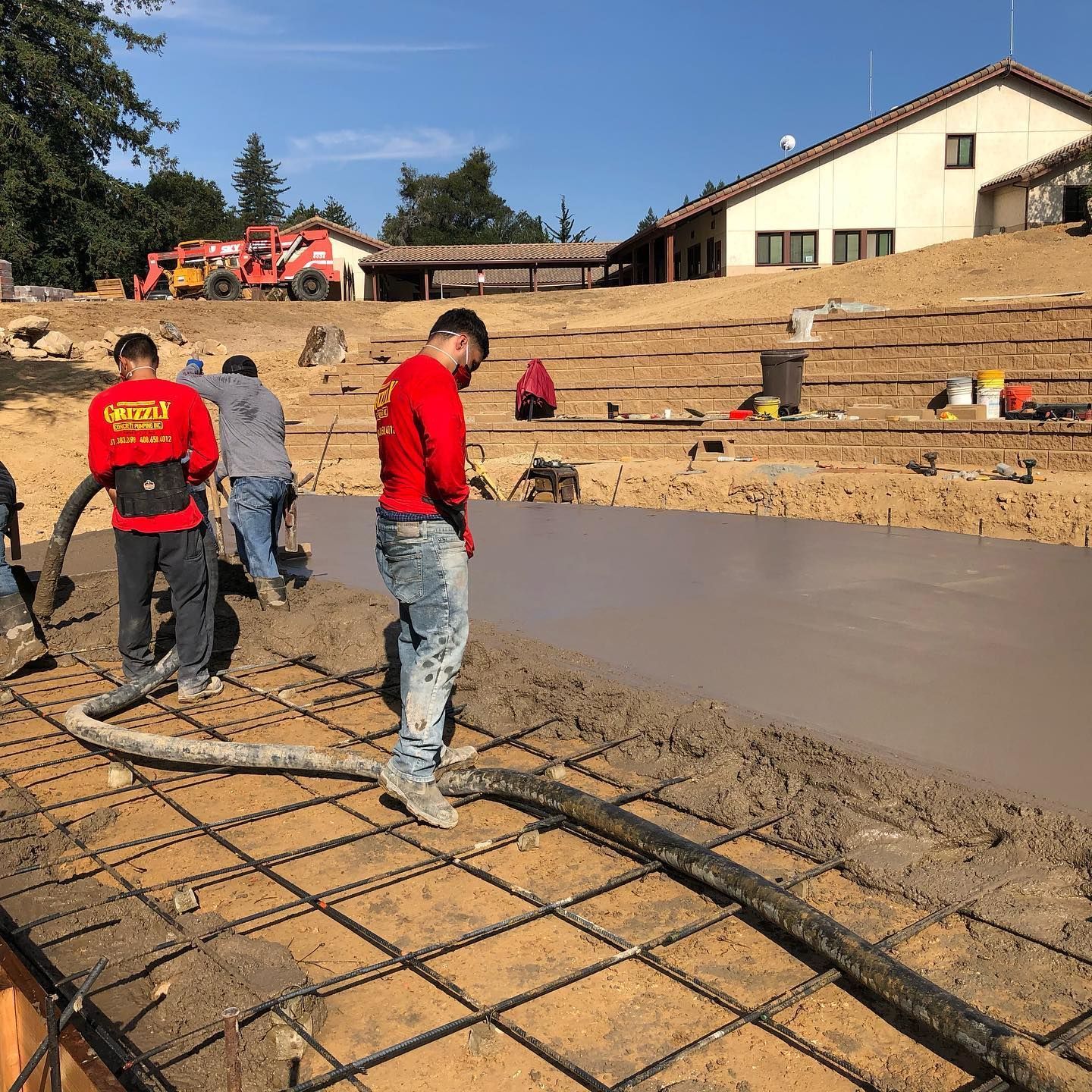 Workers in red shirts pour and smooth concrete at an outdoor construction site