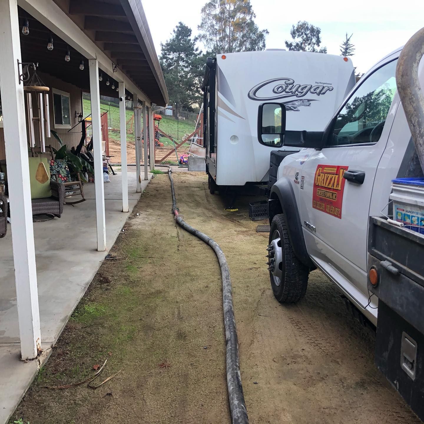 Pickup truck parked beside a house, with an RV and hose on a muddy driveway.