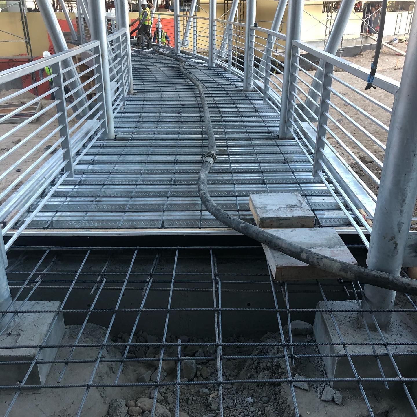Narrow metal pedestrian bridge under construction with railings and exposed rebar below