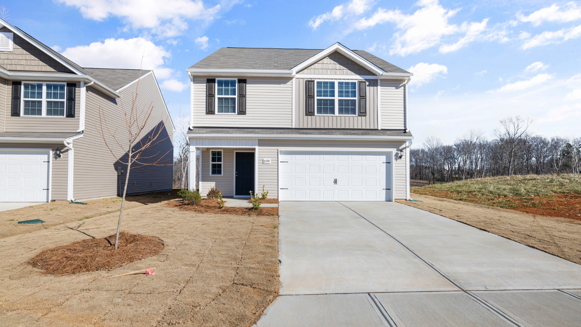 Two-story suburban house with gray siding, white garage, and a concrete driveway under a bright sky
