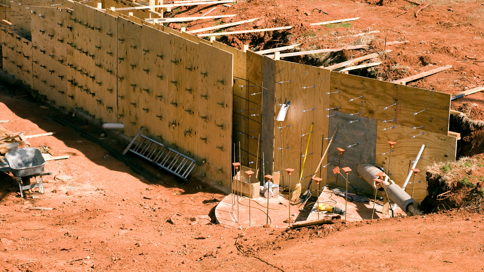 Brown earthen retaining wall with metal supports and tools on a red dirt construction site