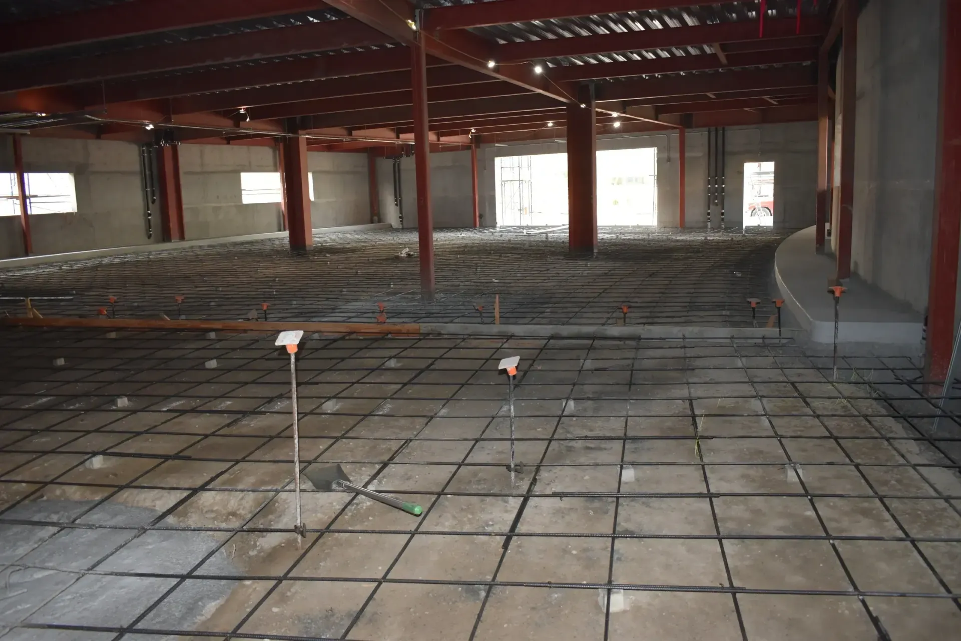 Empty warehouse interior with exposed red beams, tiled floor, and scattered construction debris