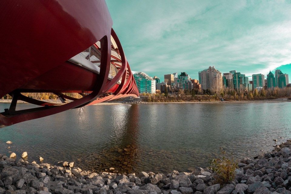 Red bridge over a river, city skyline in the background, blue sky.