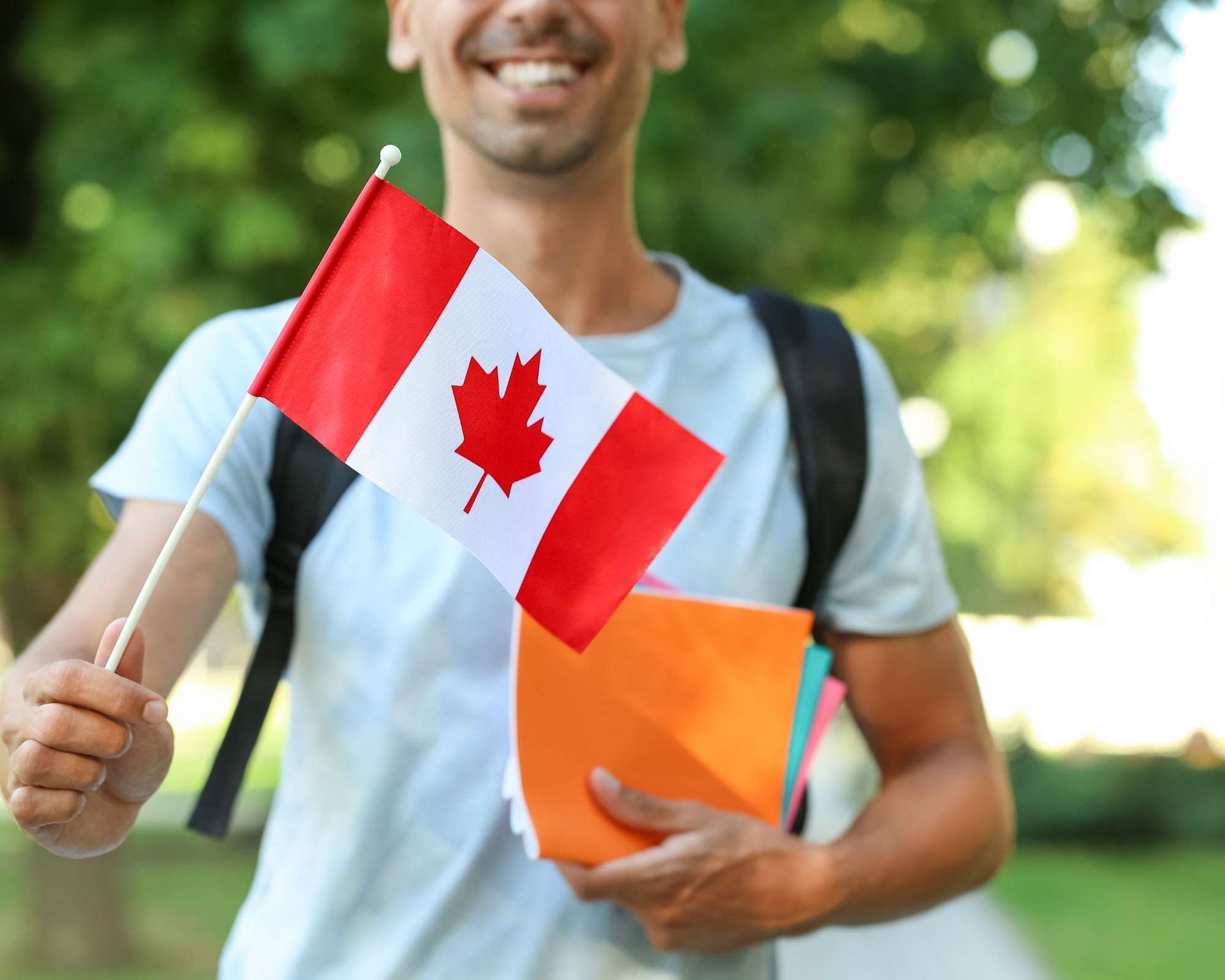 Man holding a Canadian flag and books, smiling outdoors.