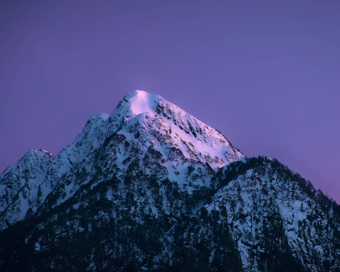 Snow-capped mountain peak under a purple and pink twilight sky.
