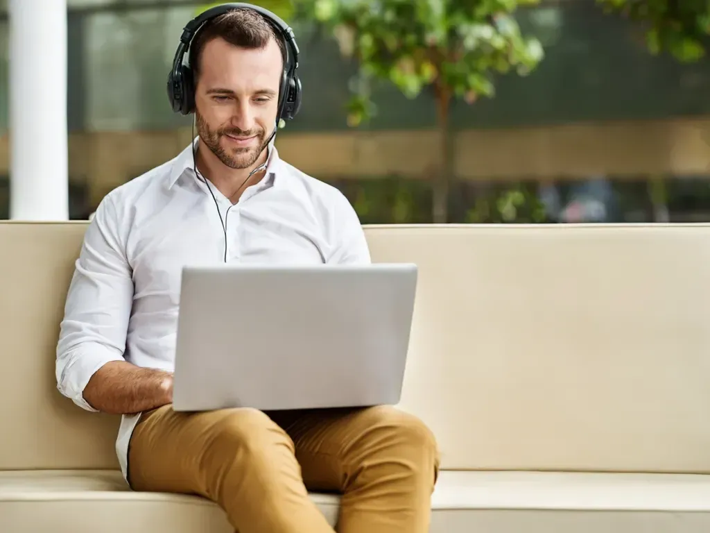 Man wearing headphones, working on a laptop while sitting outdoors.