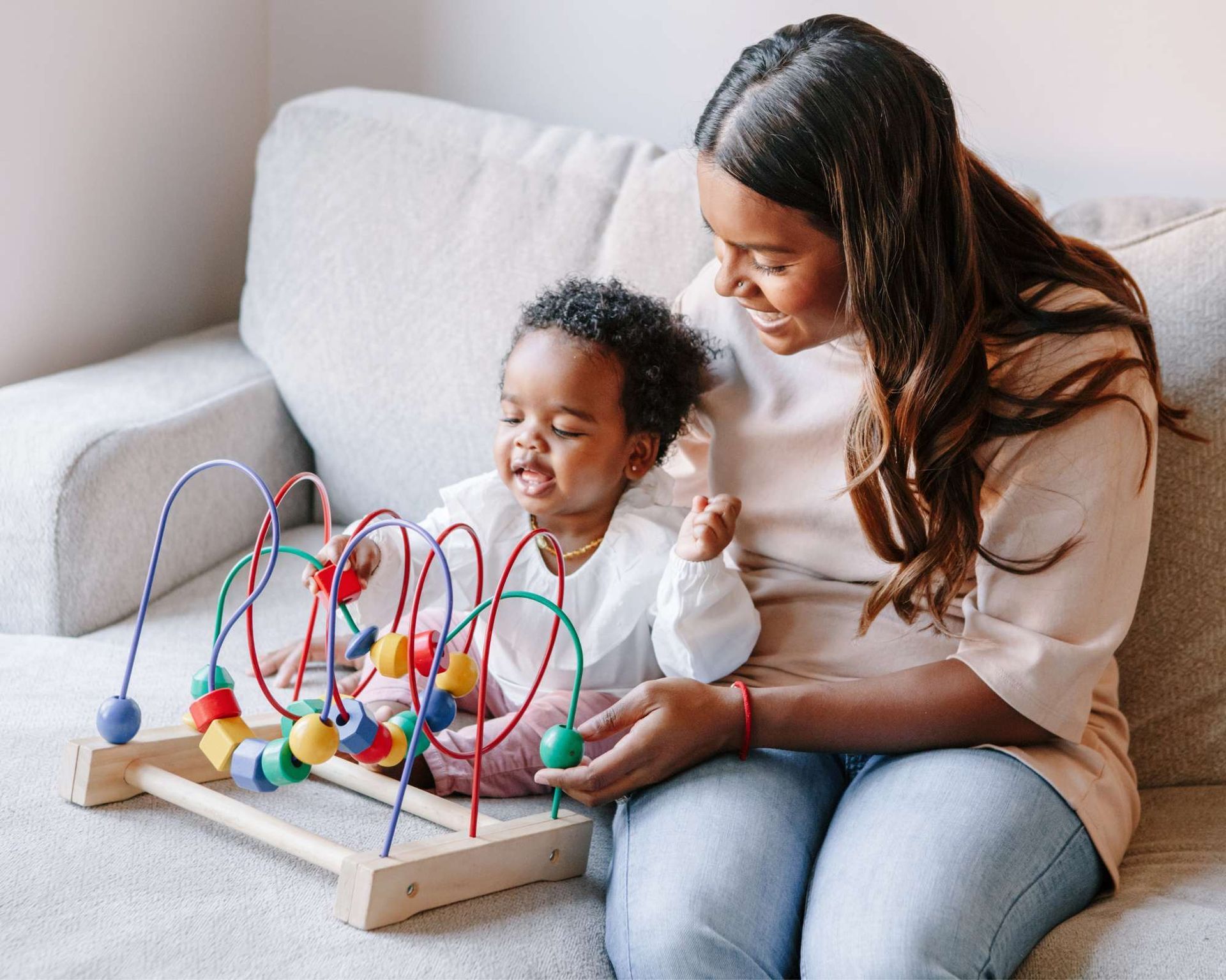 Woman and child playing with a bead maze on a couch, smiling.