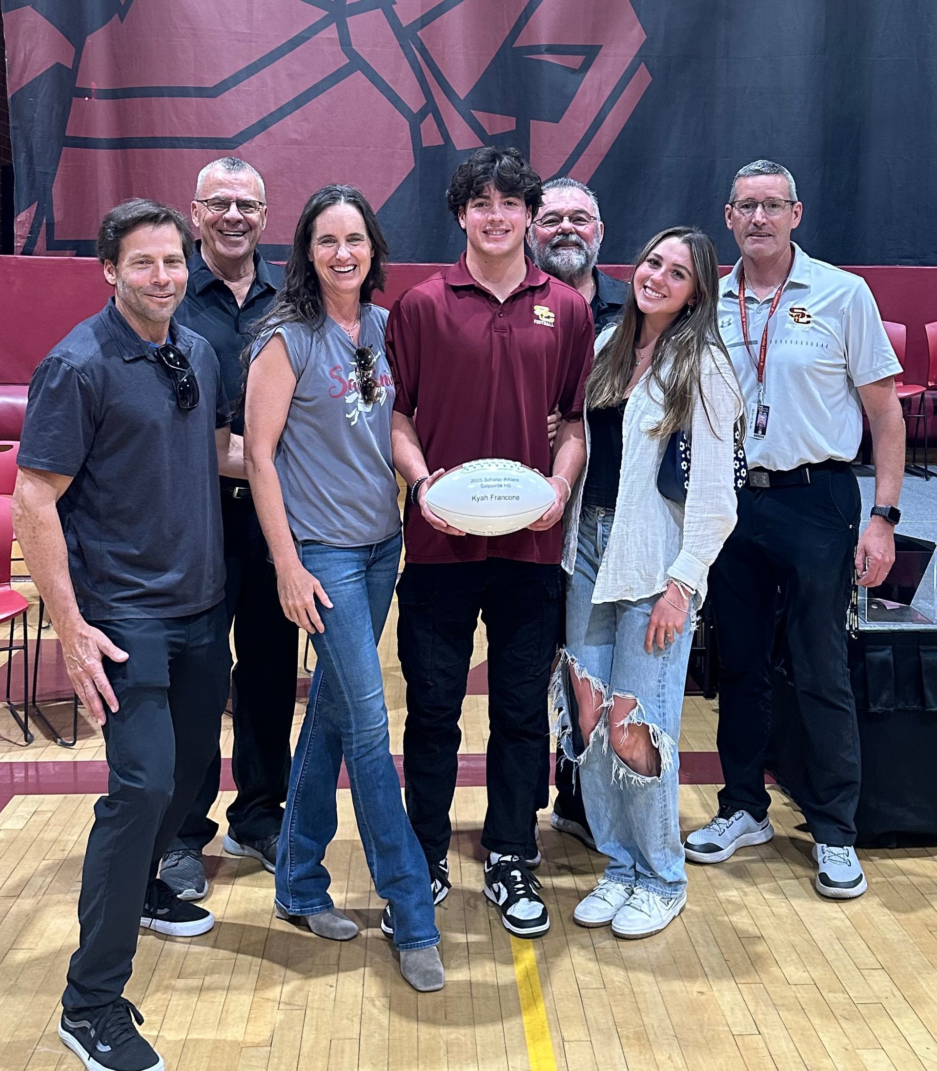 Group of people posing with a football in a gym, the person holding it is in the center.