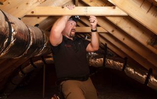 A man is working on a wooden structure in an attic.