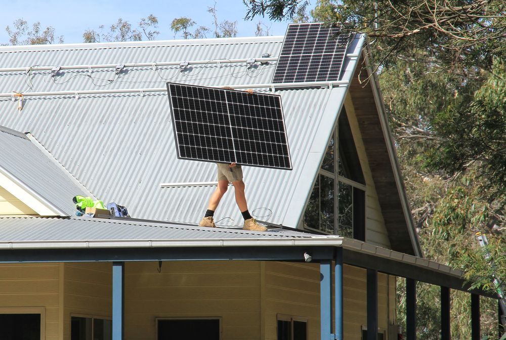 A Man is Carrying a Solar Panel on Top of a Roof — JW Electrical, Air & Solar Pty Ltd in Kempsey, NSW