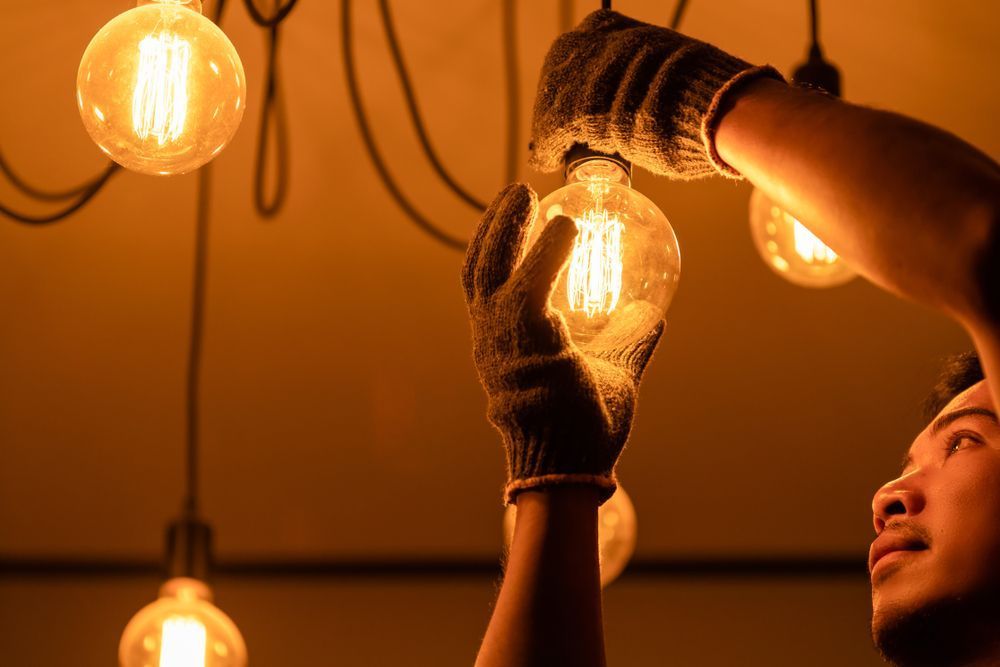 A Man is Changing a Light Bulb in a Dark Room — JW Electrical, Air & Solar Pty Ltd in Kempsey, NSW
