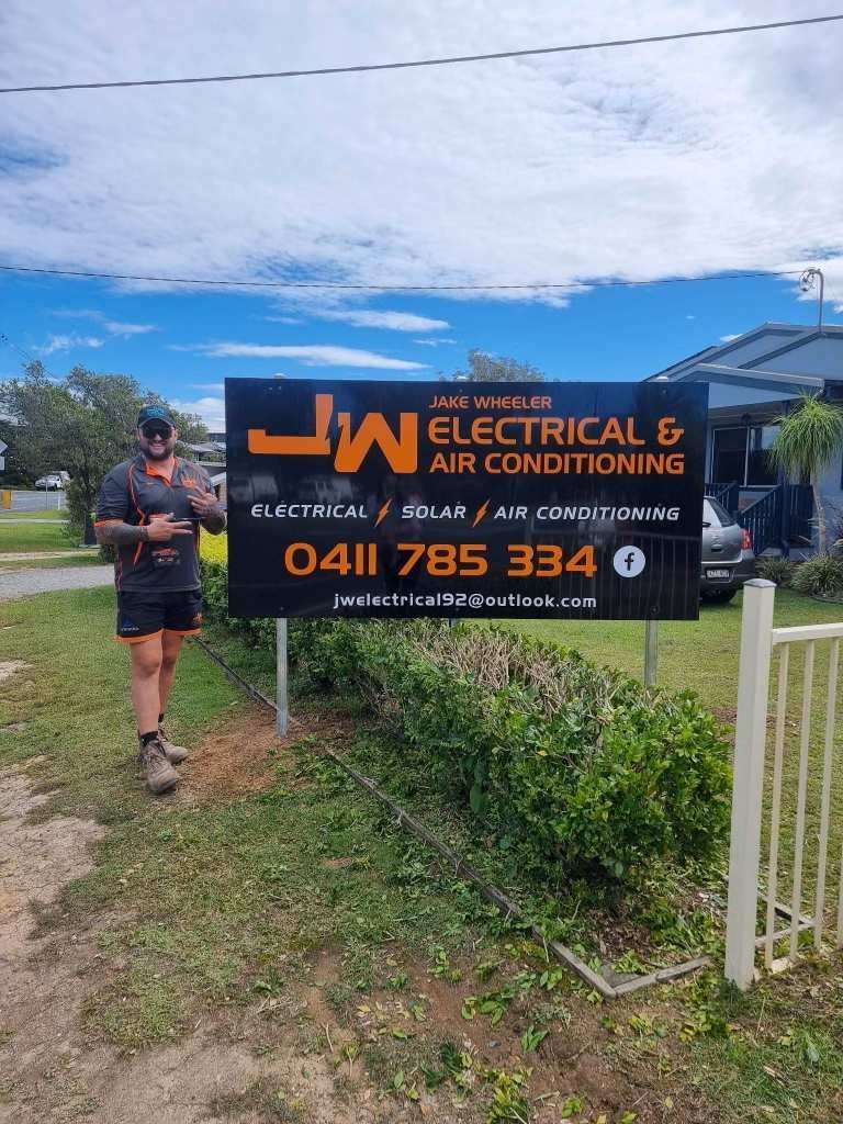 A Man is Standing in Front of a Sign for Electrical and Air Conditioning — JW Electrical, Air & Solar Pty Ltd in Kew, NSW