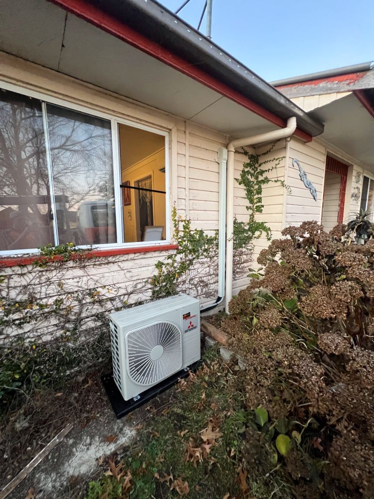 A White Air Conditioner is Sitting Outside of a House Next to a Window — JW Electrical, Air & Solar Pty Ltd in Kew, NSW