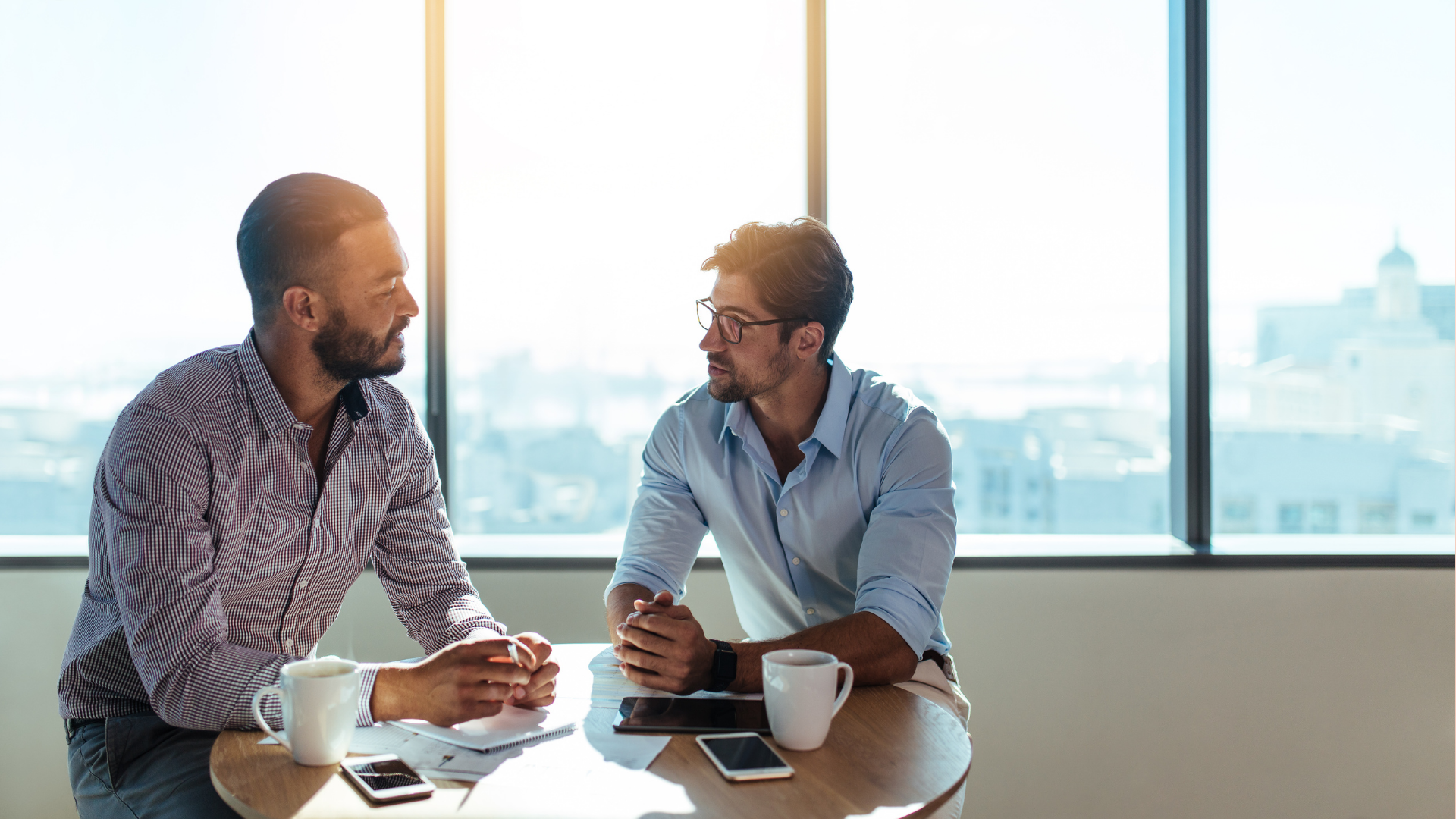 Two men are sitting at a table talking to each other.