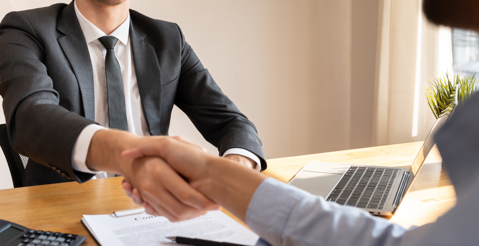 Business handshake over a desk with a laptop and paperwork