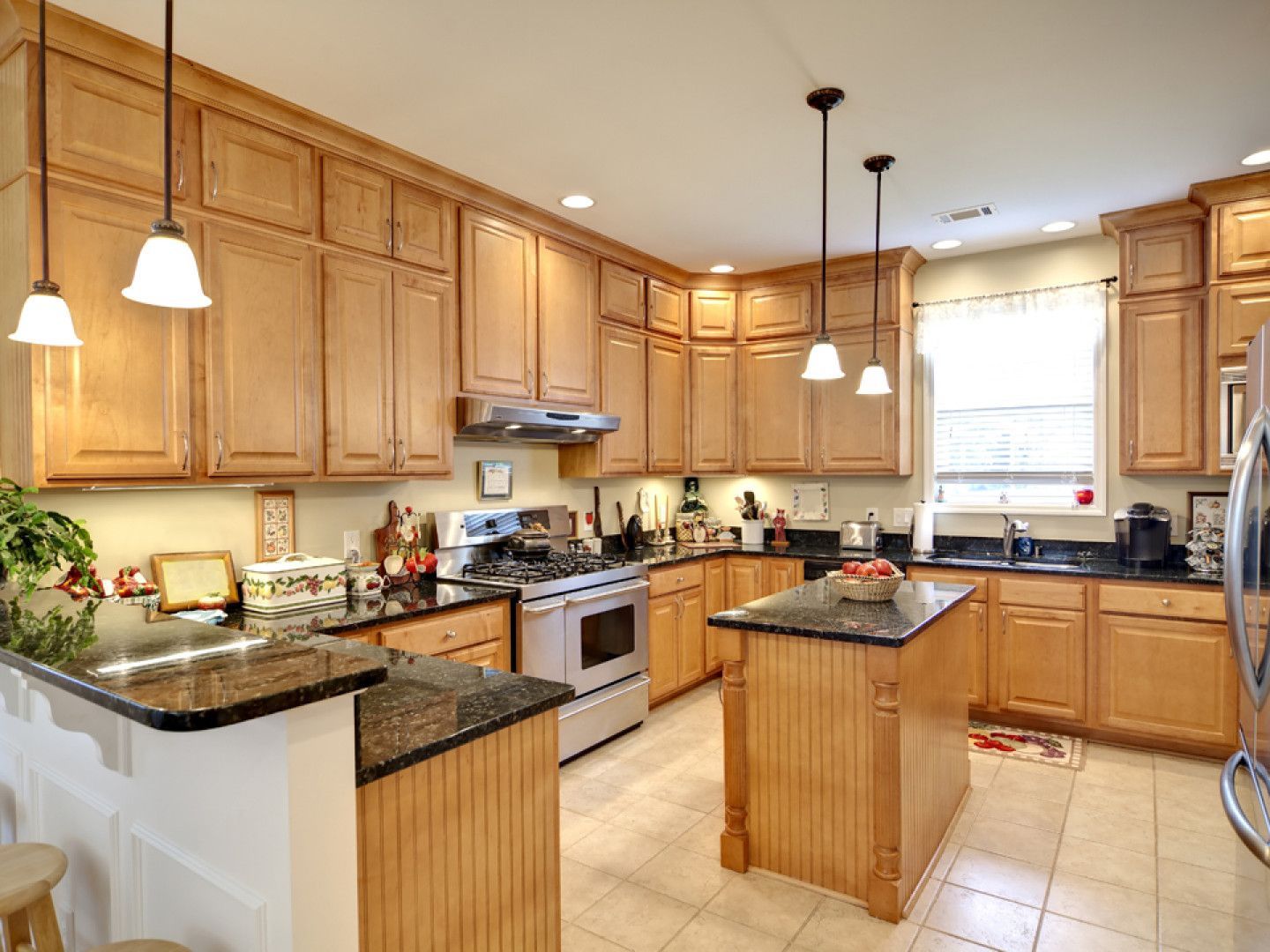 A well-lit kitchen with wooden cabinets, black countertops, and a central island.