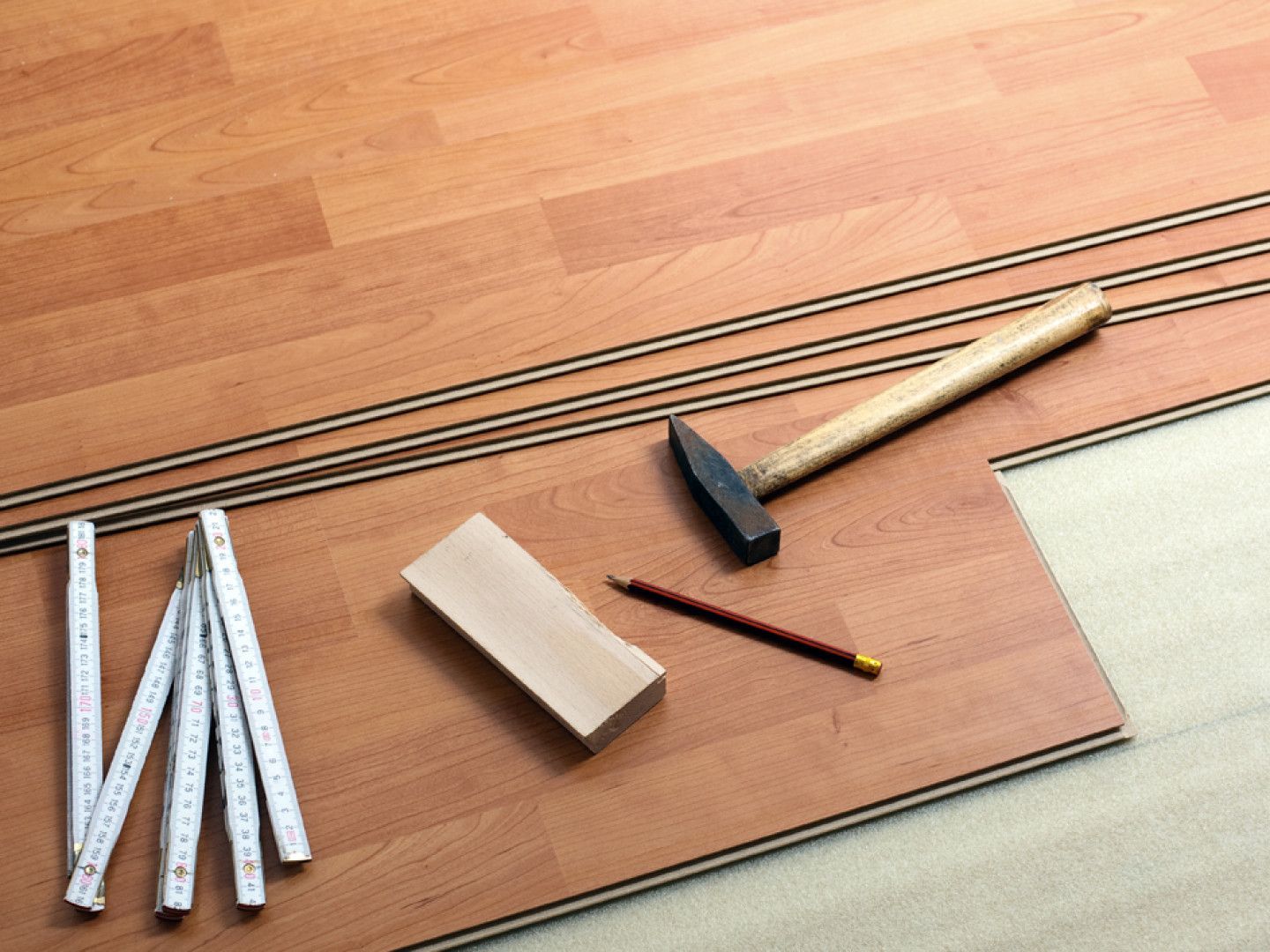 Laminate flooring installation with hammer, pencil, ruler, and wood block.