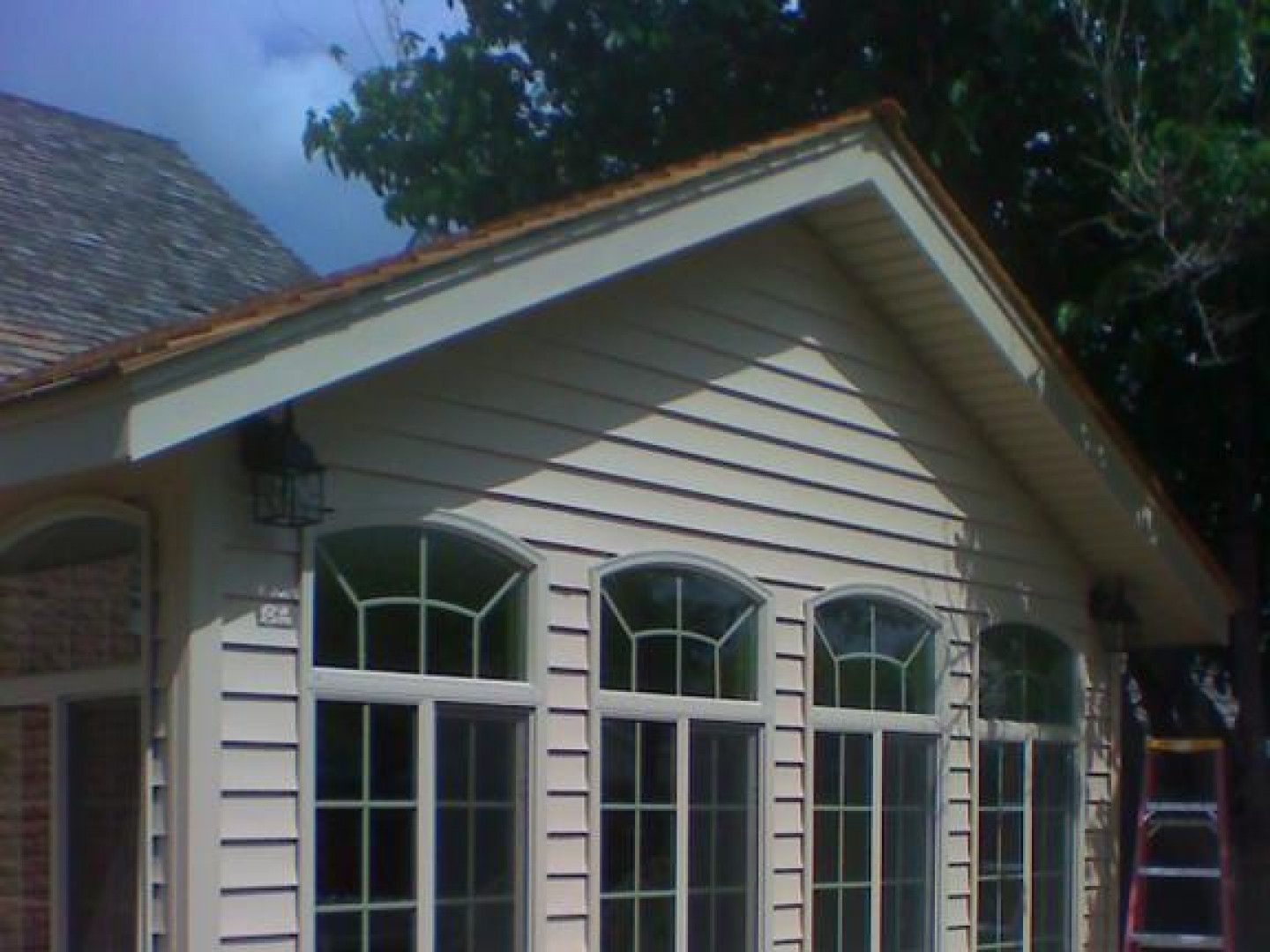 Beige siding house with arched windows and brown trim under a partly cloudy sky.