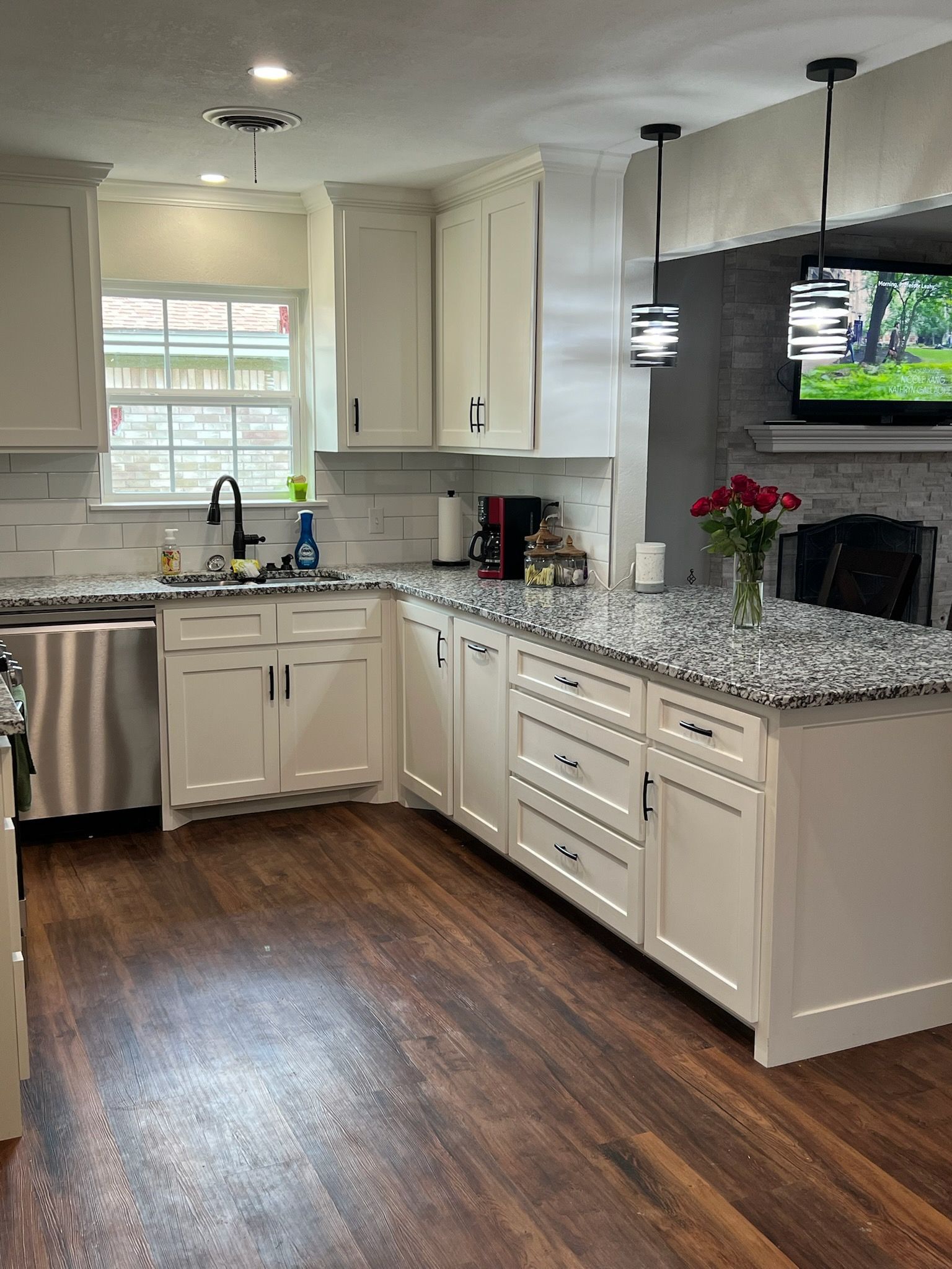 Bright white kitchen with granite countertops, wood floors, and island. Includes sink, cabinets, appliances, and a window.
