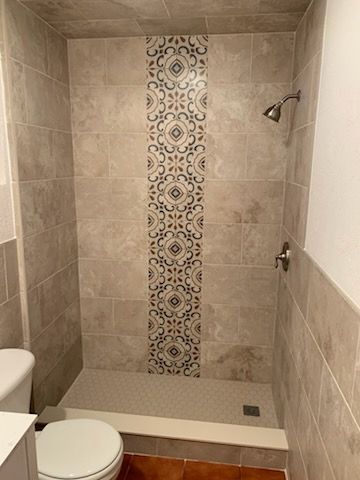 Shower with beige tiles, decorative center strip, and toilet.