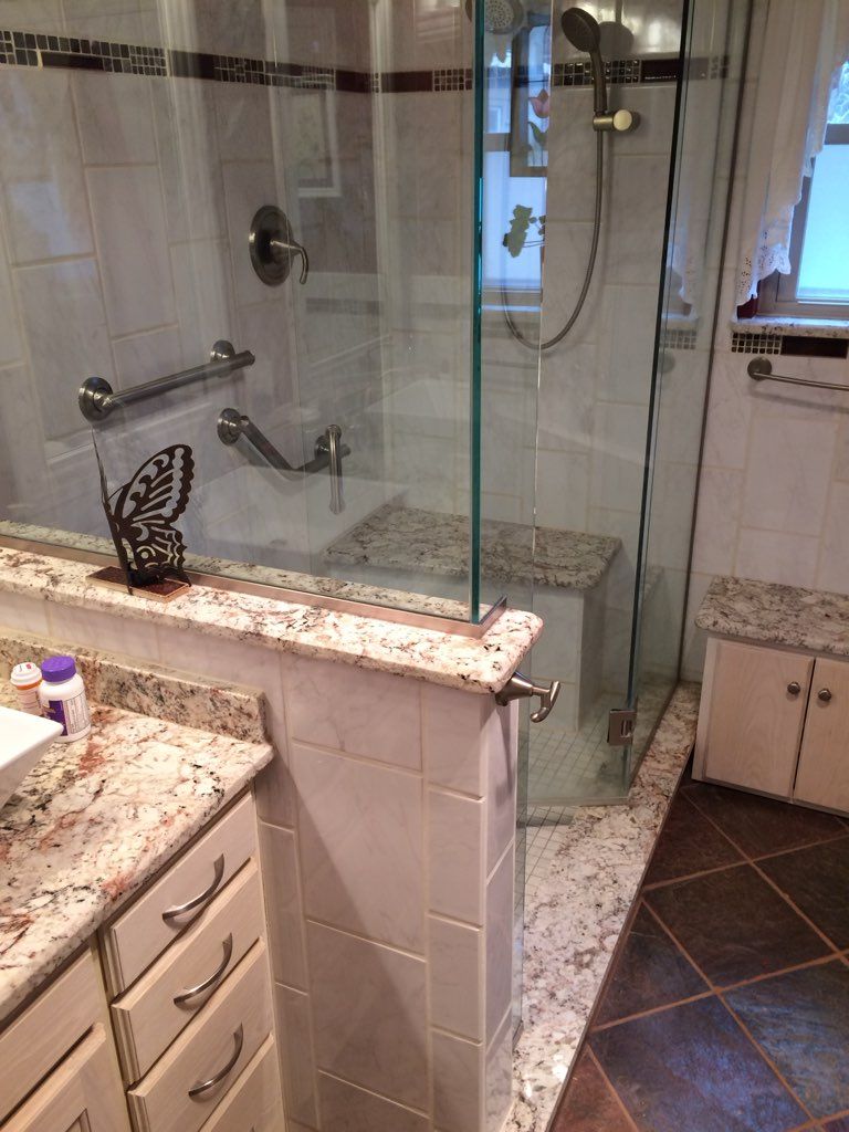 Bathroom with glass shower, granite countertops, tile, and grab bars.