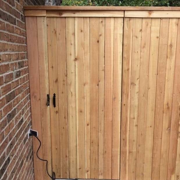 Wooden gate built into a brick wall, closed, with black handles.