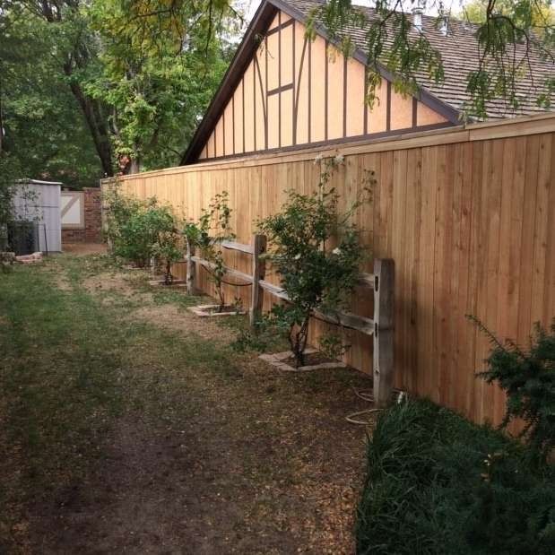 Wooden fence along a yard with a house in the background and rose bushes.