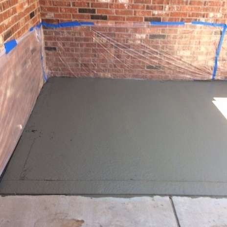 Freshly poured gray concrete floor next to a brick wall, covered with protective plastic.