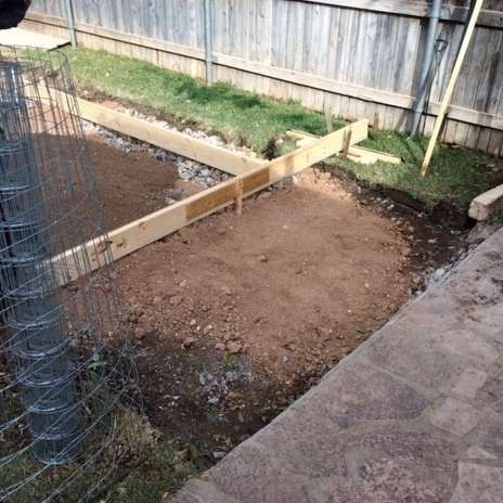 Wooden frame outlining a dirt area; construction in a backyard, fence in the background.