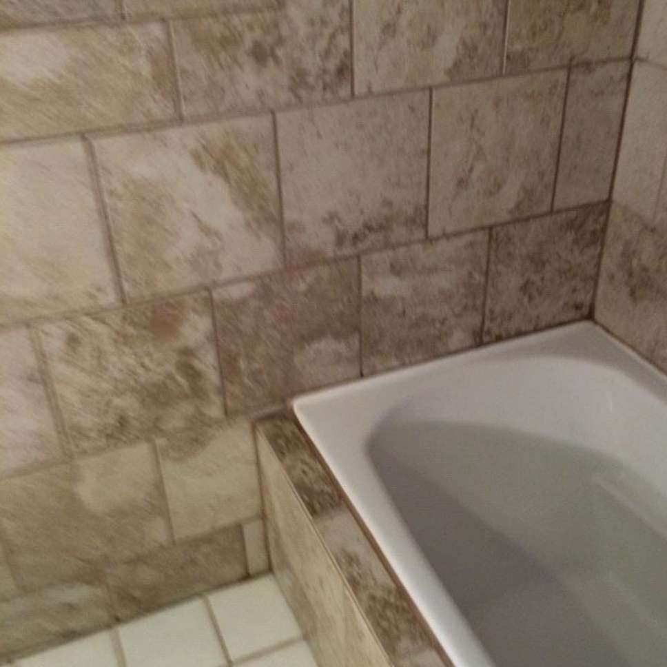 Bathroom with tan-colored tiled walls and a white bathtub. The floor tiles are off-white.