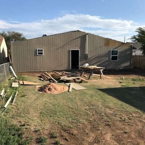 Backyard with unfinished house exterior, lumber, and a small pile of dirt.