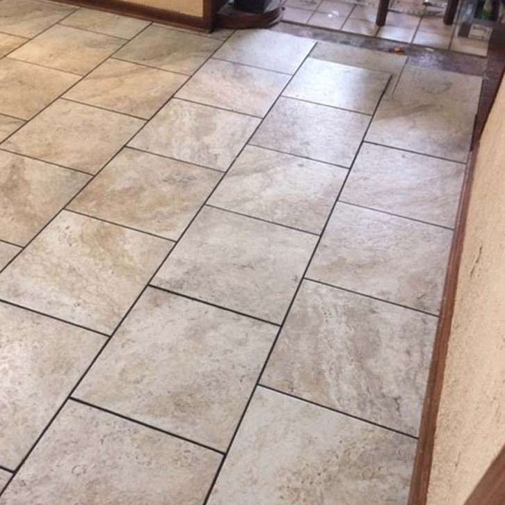 Tiled floor with beige rectangular tiles, black grout lines, near a wooden trim.