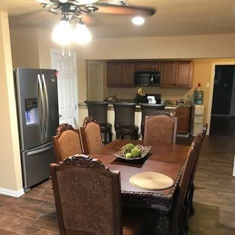 Dining room with a wooden table and chairs, connected to a kitchen with a refrigerator and microwave.