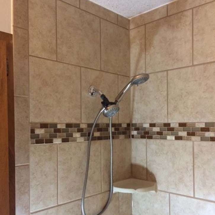 Tiled shower with a hand-held showerhead and corner shelf. Beige and brown tiles.