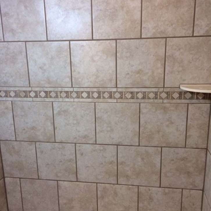 Beige tile wall with decorative border and small shelf.