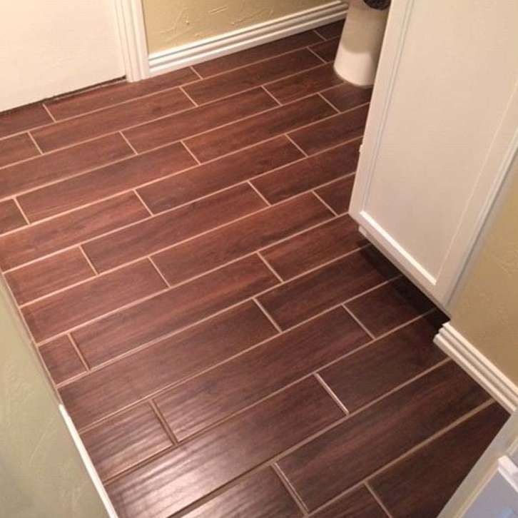 Bathroom floor with dark brown wood-look tile laid in a staggered pattern. White door and cabinet visible.