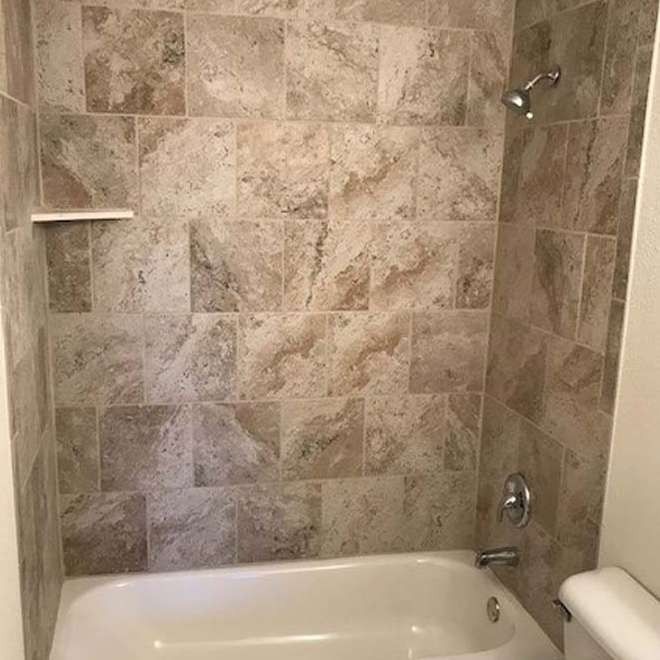 Tiled shower stall with a white bathtub and silver shower fixtures. Beige tiles cover the walls.
