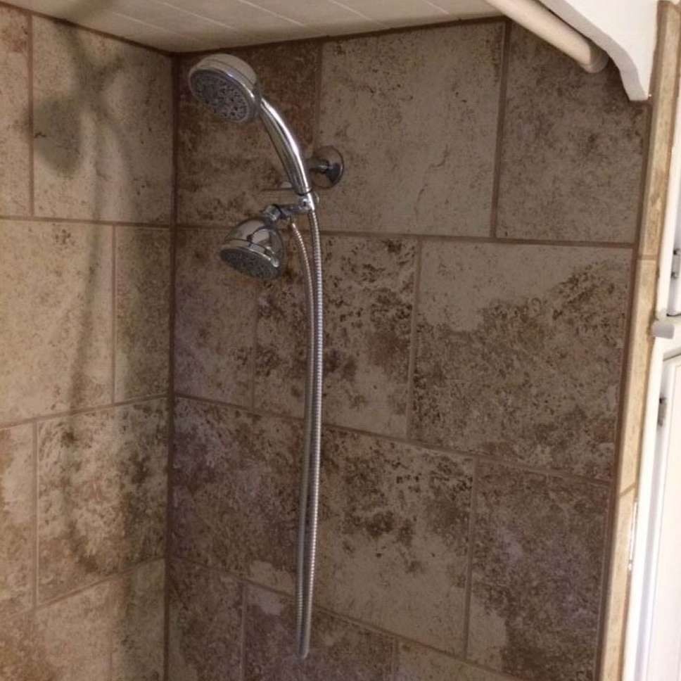 Shower with handheld showerhead on tiled wall.