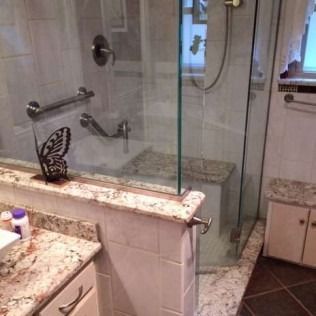 Bathroom with glass shower, grab bars, marble countertop, and a built-in seat.